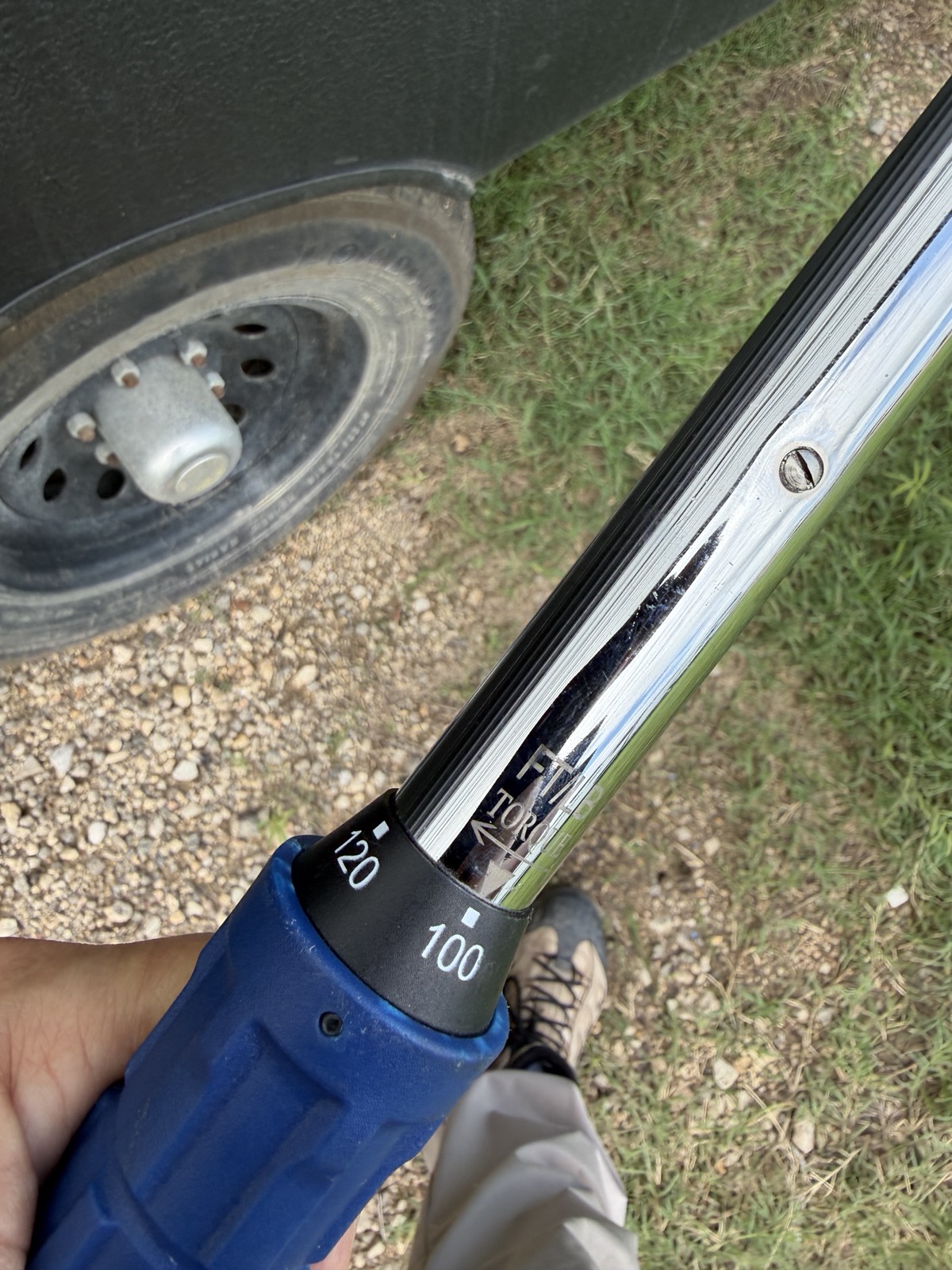 Close-up of torque wrench handle showing 100/120 ft-lb scale with trailer wheel in background