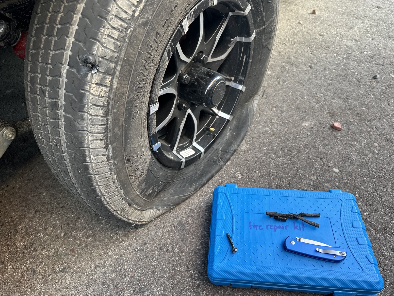 Flat trailer tire with plug repair kit open on the ground — found and repaired at pre-trip inspection