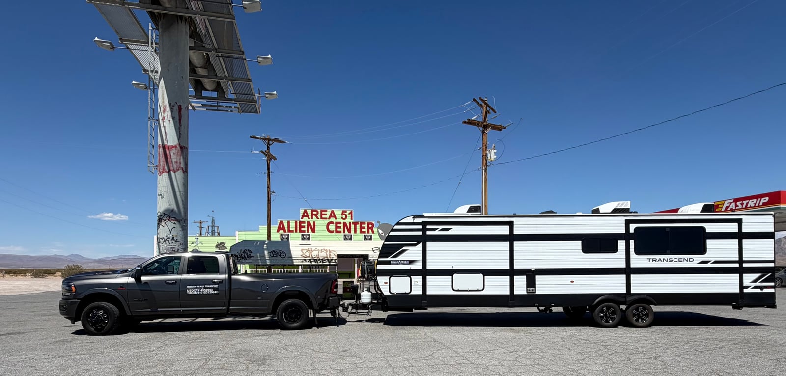 Mission Ready Transport truck towing a Transcend travel trailer at a roadside stop in the desert