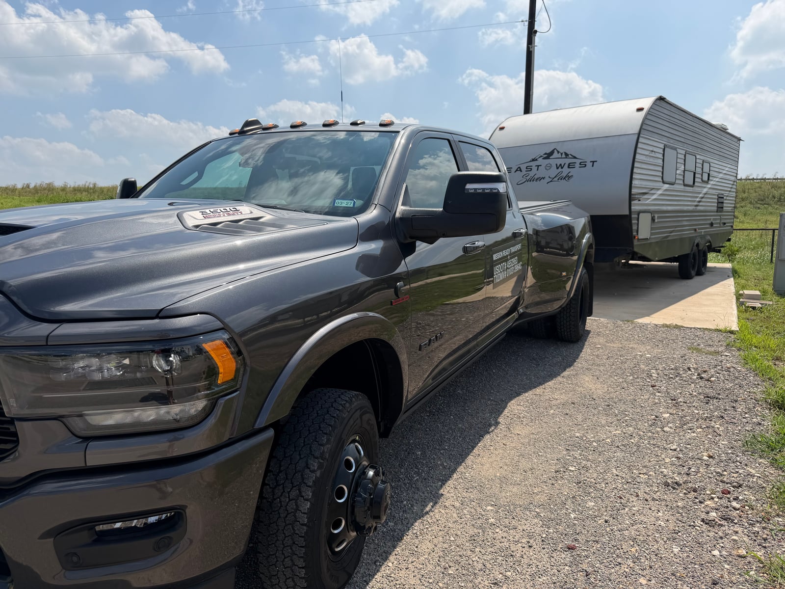 Mission Ready Transport truck towing an East to West Silver Lake travel trailer up a gravel driveway