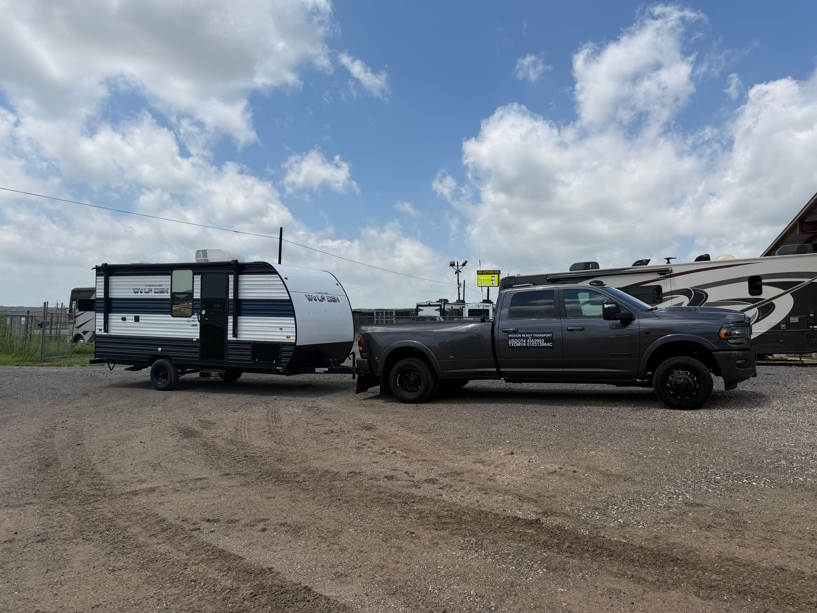 Mission Ready Transport truck towing a compact travel trailer off a gravel lot