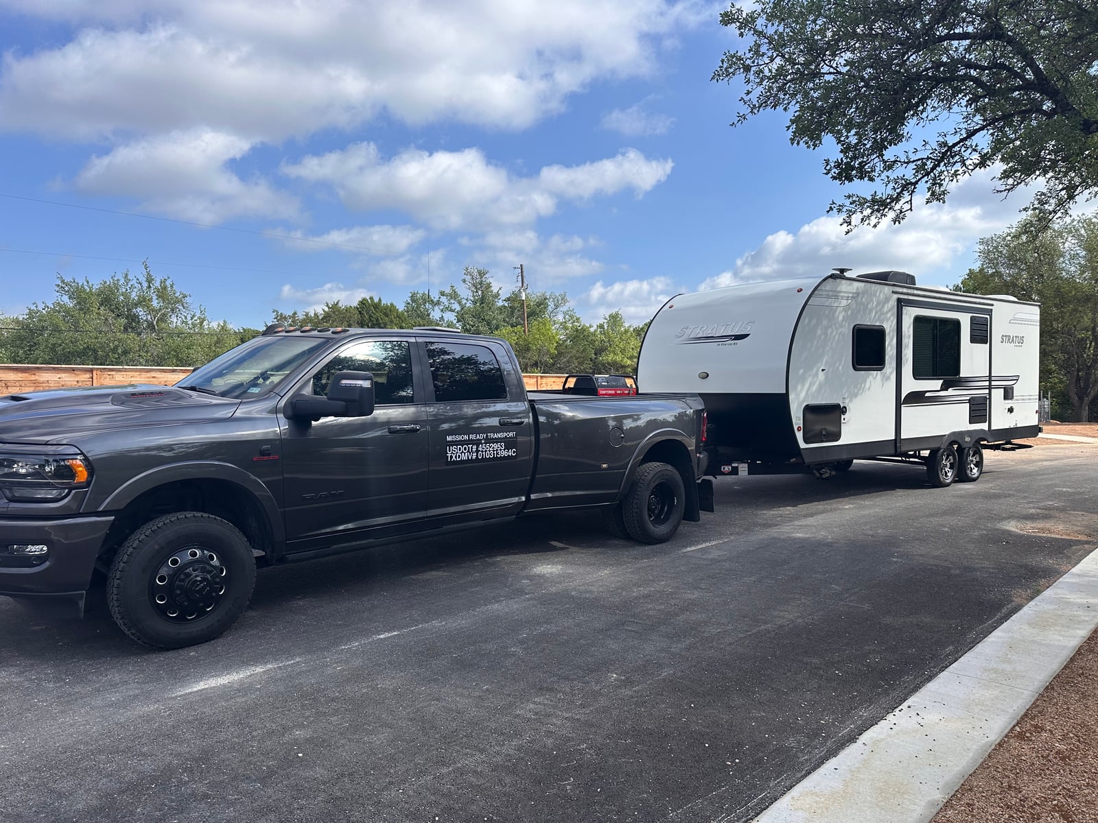 Mission Ready Transport truck towing a white travel trailer down a freshly paved lane