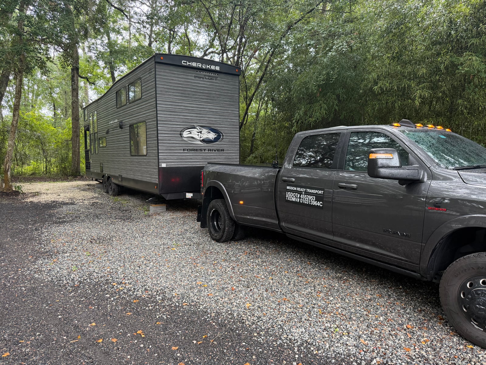 Mission Ready Transport truck towing a Forest River Cherokee travel trailer out of a wooded lot